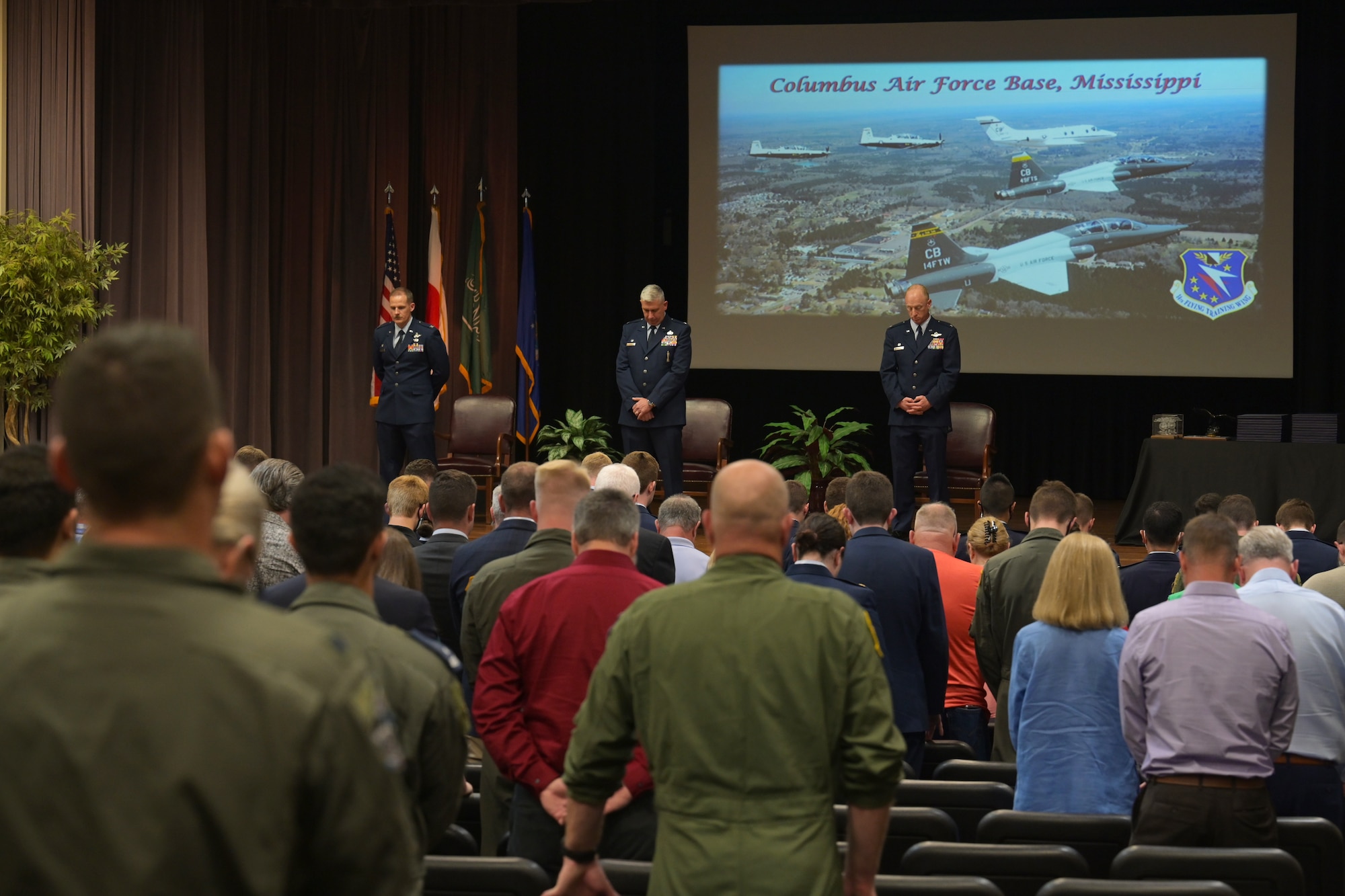 The official party and audience members attending the graduation of Specialized Undergraduate Pilot Training class 21-10 lower their heads in prayer May 27, 2021, on Columbus Air Force Base, Miss. The 21 graduates completed a 52-week pilot training program including academics, physiological training, and flight training in the T-6A Texan II, T-1A Jayhawk, and T-38C Talon. (U.S. Air Force photo by Senior Airman Jake Jacobsen)