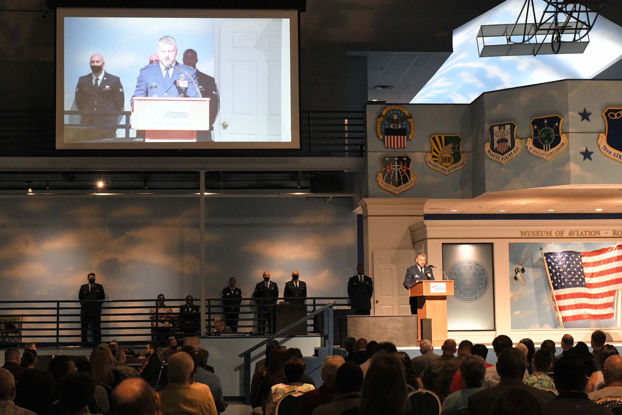 Photo shows a man standing at a podium with seated crowd in front of him.