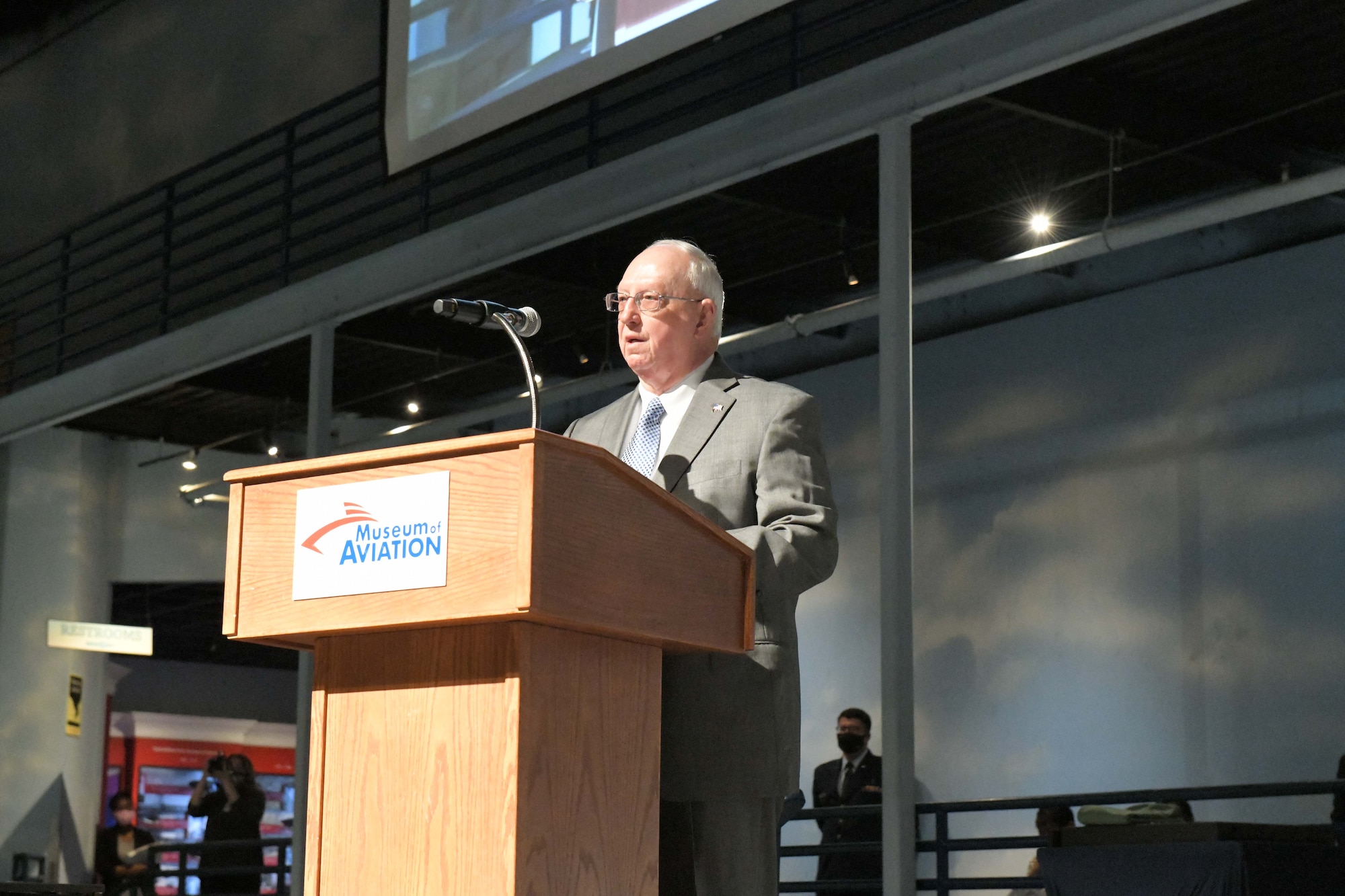 Photo shows man standing at podium.