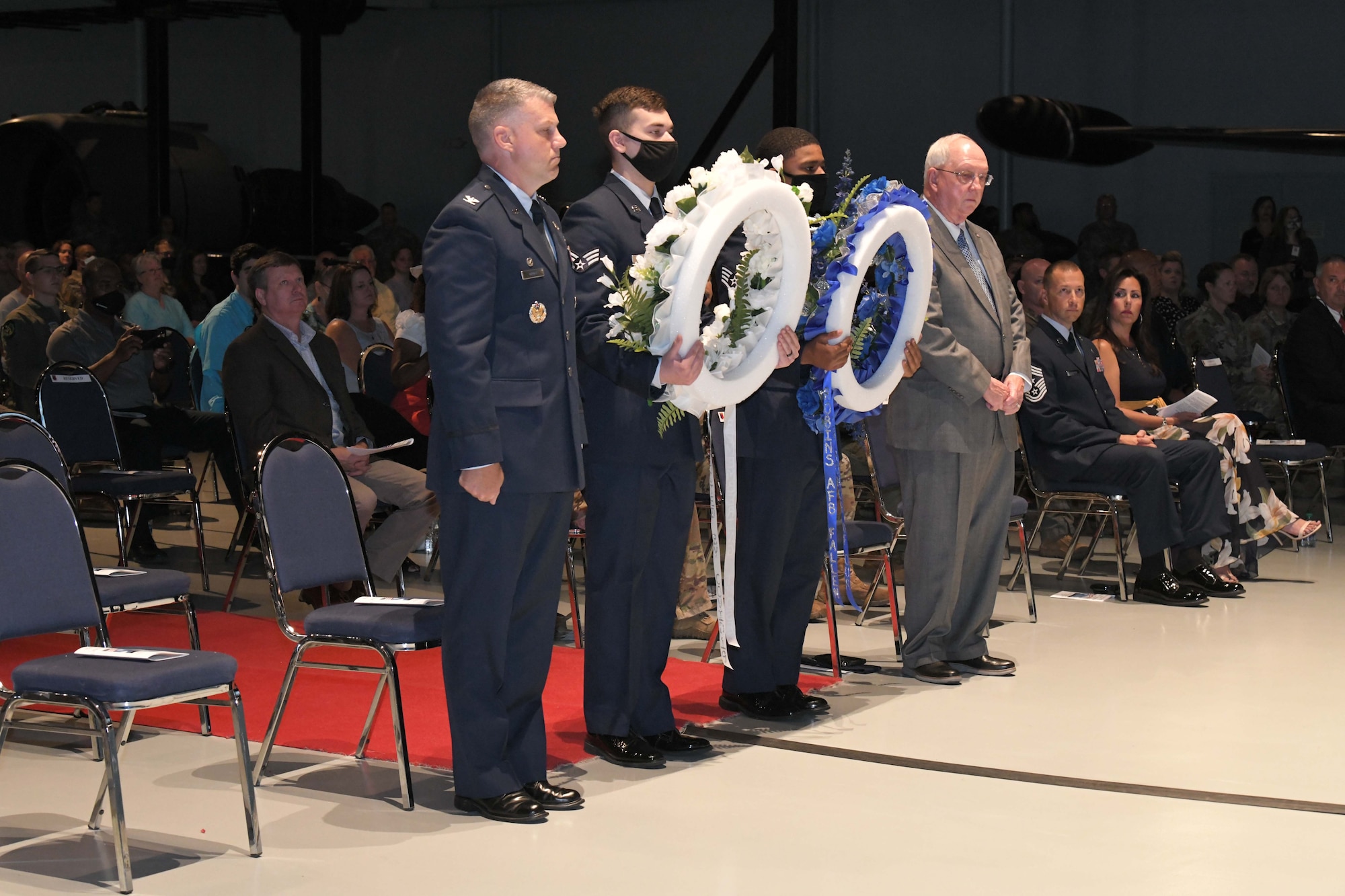 Photo shows four men standing in line holding two wreaths.