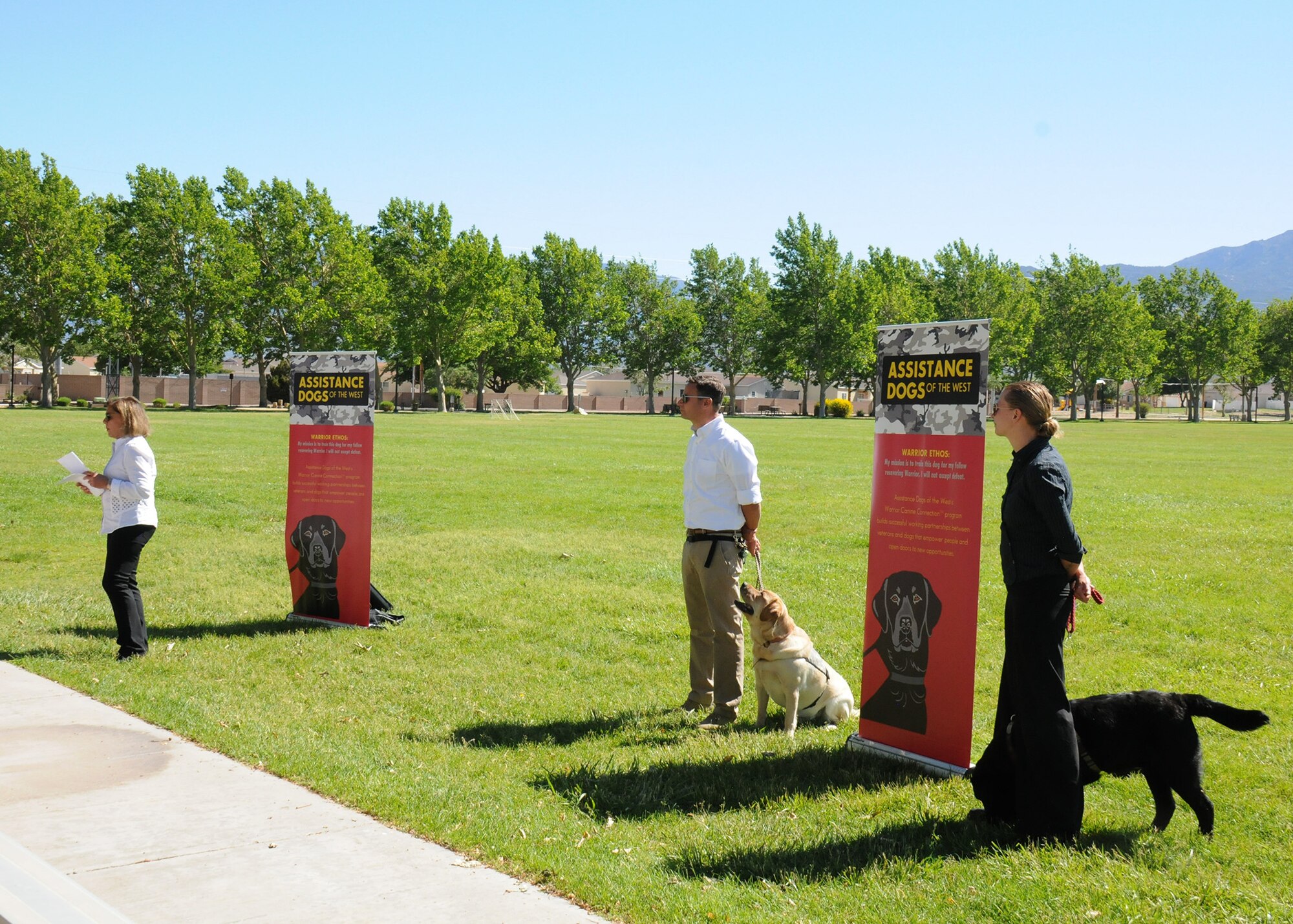 Two women and one man give a presentation outdoors about service dogs.