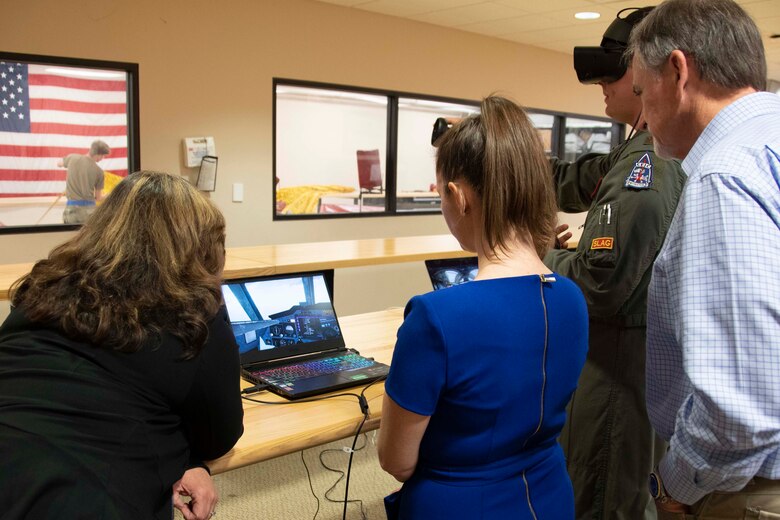 Civilians look at a computer screen while a pilot explains the virtual reality training system.