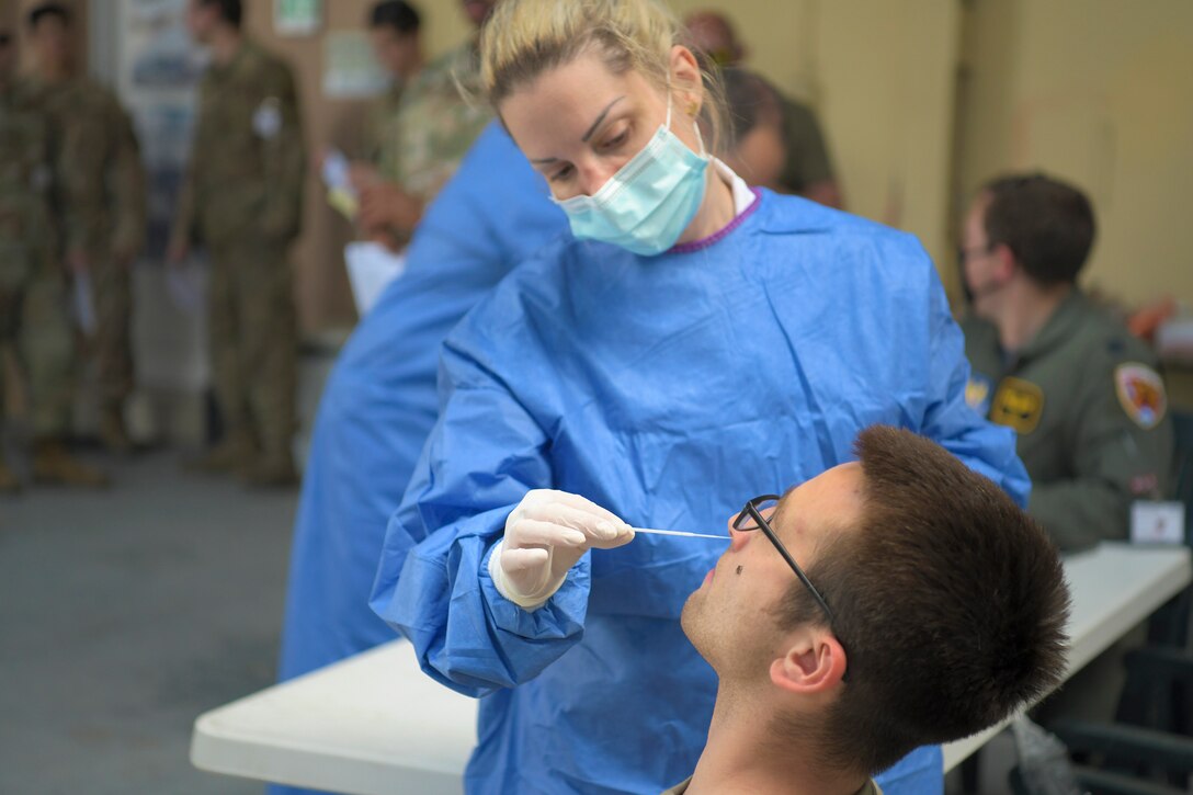 A woman inserts a swab into the nostril of an airman.
