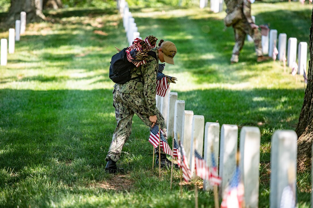 Service members place flags on headstones.