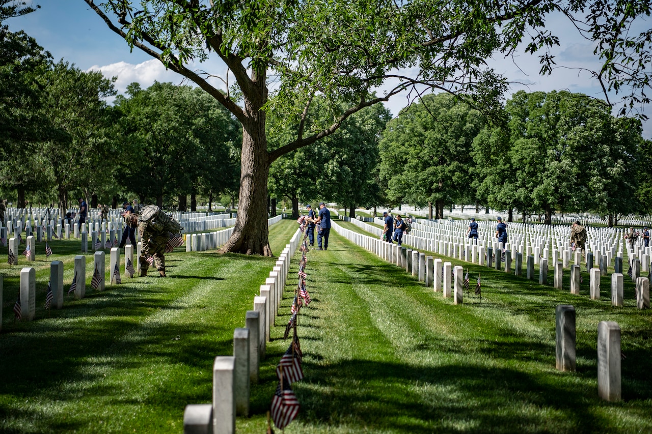 Service members place flags on headstones.