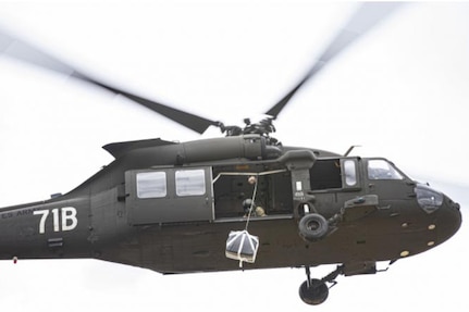 A helicopter flies while a crew member inside the helicopter prepares an emergency re-supply drop.