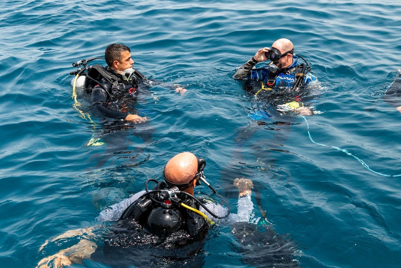 Military personnel float near each other in the water while wearing equipment that allows them to breathe underwater.