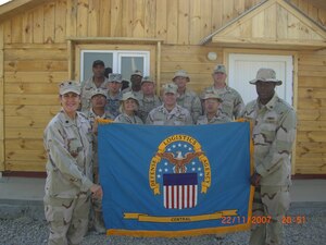 A group of men and women in BDUs hold up a flag for DLA  Contingency Support Team Afghanistan.