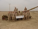 A group of men and women in BDUs pose in front of a tank in Afghanistan.