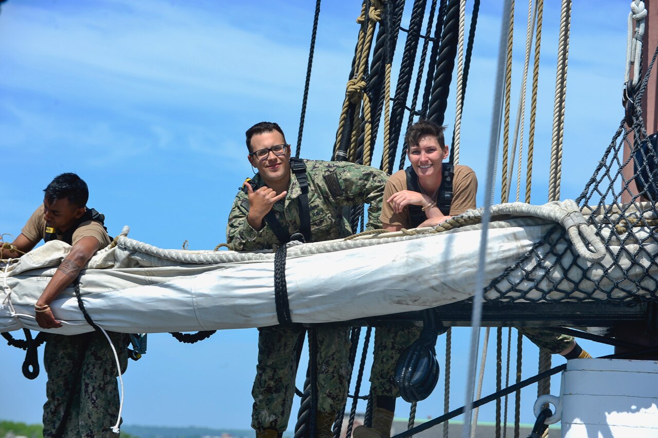 Two sailors perched high atop a historic three-masted frigate smile for a photo.