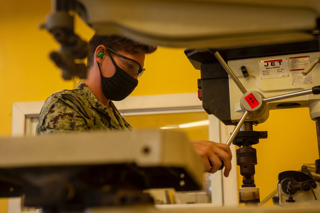 A sailor in a face mask performs work on a machine.