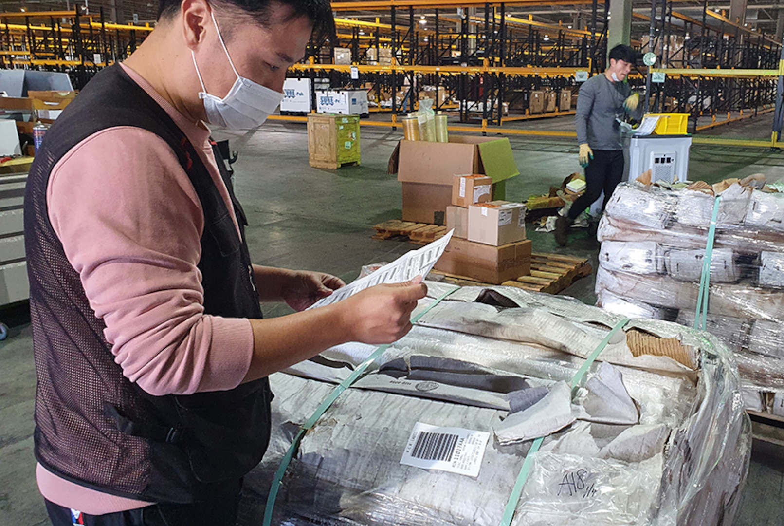 A material examiner looks over paperwork in a warehouse.