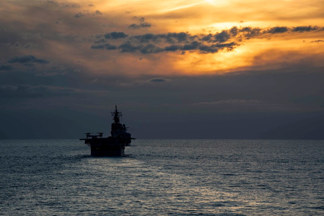 A ship transits a body of water under a sunlit sky.