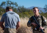 Man holding a weapon listens to another man giving instructions.