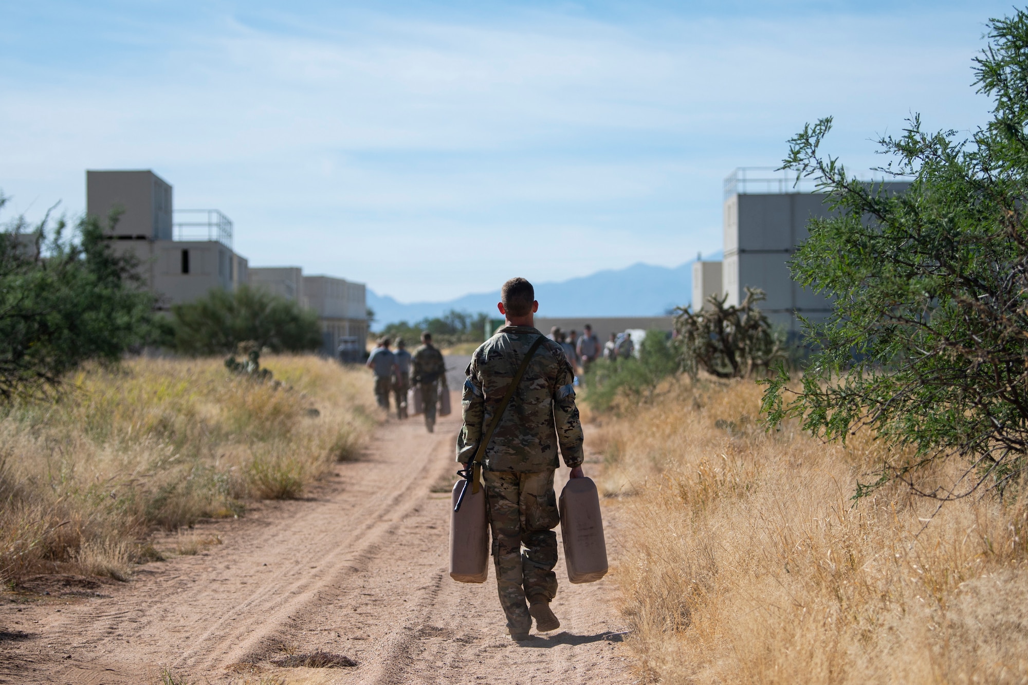 Person carrying a "jerry can" walks down a dirt road.