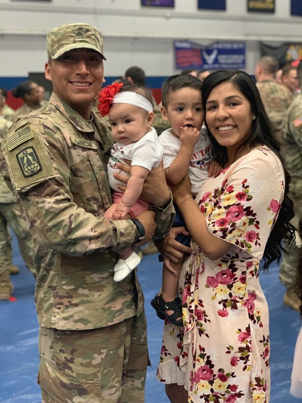 A man in a uniform holds a small child.  Next to him is a woman who is also holding a small child.