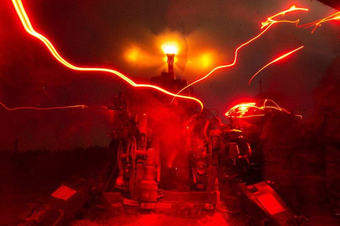 Red beams of light illuminate the sky as a howitzer fires.