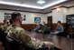 Military members in uniform sit in a room talking.