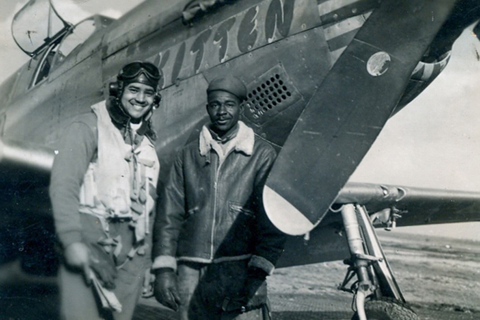 A soldier poses for a photo next to an aircraft with his friend.