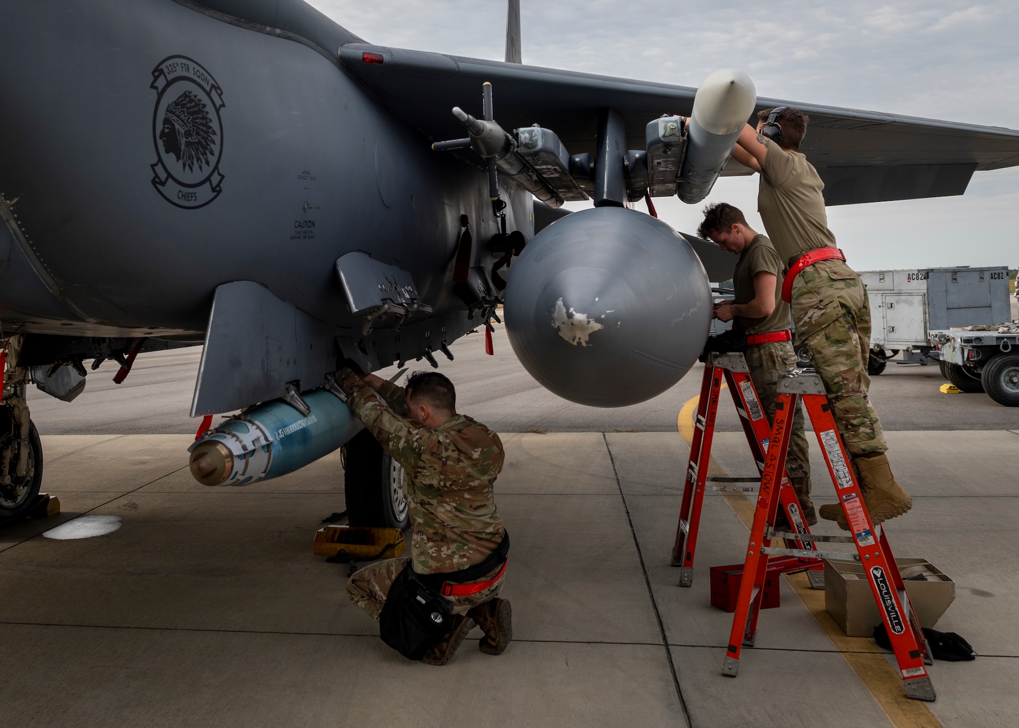 The load crew two and three men, right, install the aim-120 missile wings and fins and the load crew team chief, left, connects the 1760 smart weapons cable to the GBU-38 onto an F-15E Strike Eagle during a quarterly load crew competition at Seymour Johnson Air Force Base, North Carolina, Oct. 21, 2021.