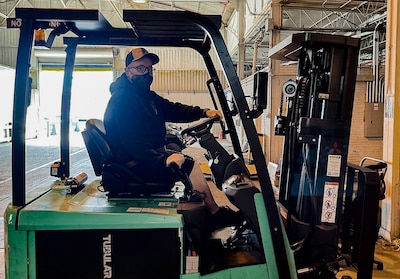 A man operates a forklift inside a warehouse.