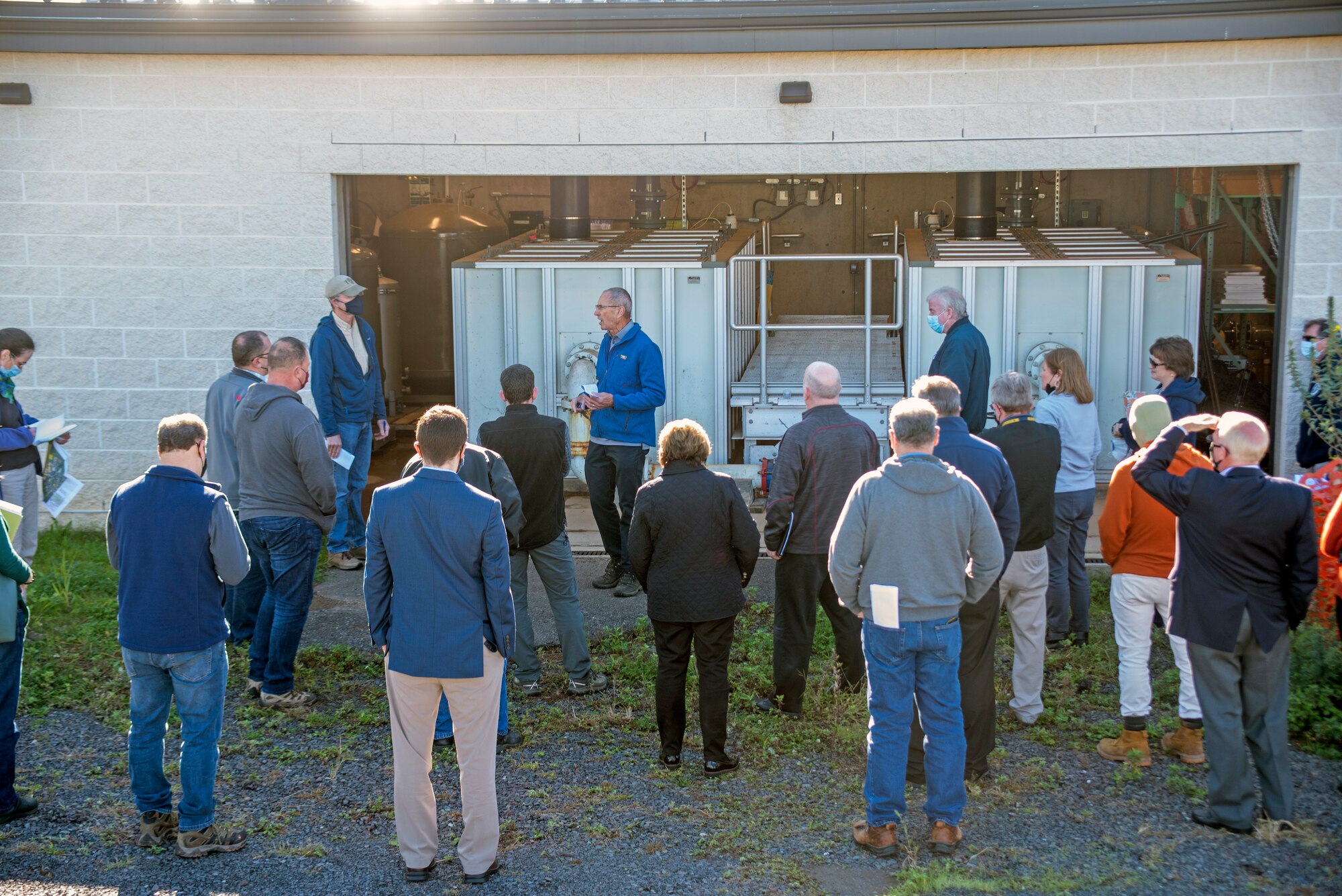 A man briefs a crowd in fron of a water treatment plant.