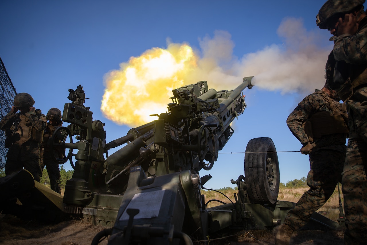 Marines fire a howitzer in a field.