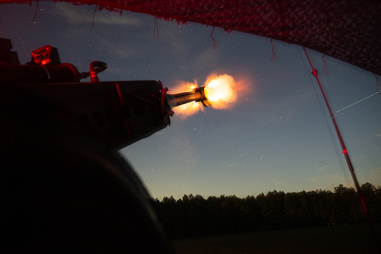 Marine fire a howitzer at night in a field.