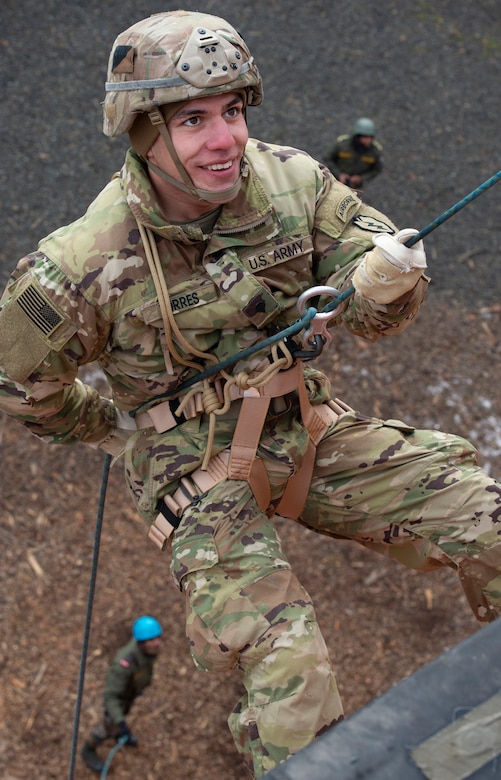 An Army paratrooper rappels down a wall.