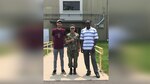 Two men in civilian clothes and one woman in military fatigues stand together outside of a building.