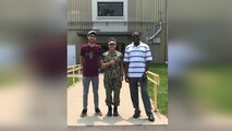 Two men in civilian clothes and one woman in military fatigues stand together outside of a building.
