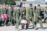A little girl in a flight suit and pink tutu marches in an outdoor formation with cadets also in flight suits.