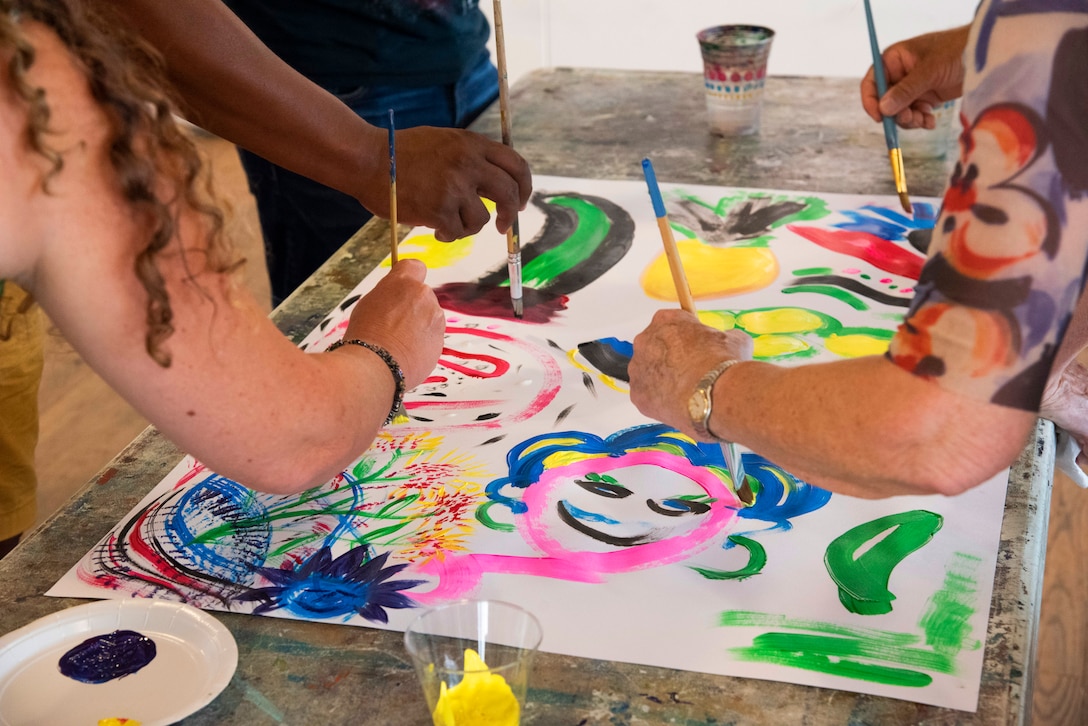 Recovering service members and staff work on a painting together during an art clinic.