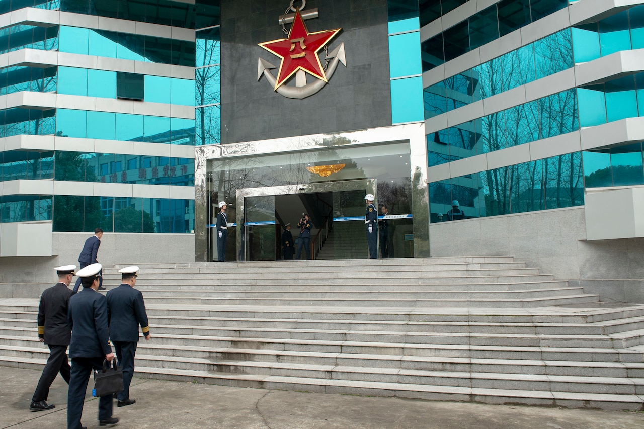 Men in military uniforms approach steps in front of a building.