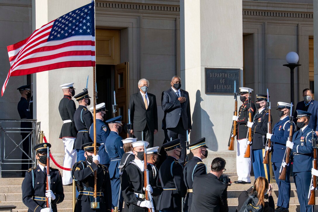 Defense secretary and another official stand on Pentagon steps, flanked by honor guard troops.