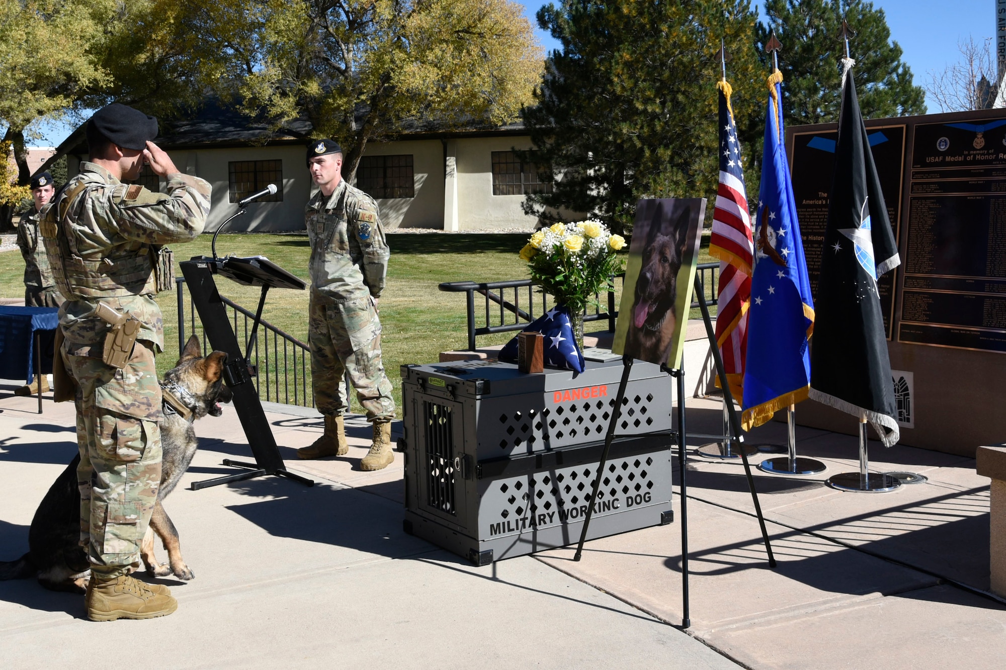 Staff Sgt. Logan Franks, 21st Security Forces Squadron military working dog handler, and MWD Ben, salutes fallen MWD Rexo’s display during his memorial ceremony