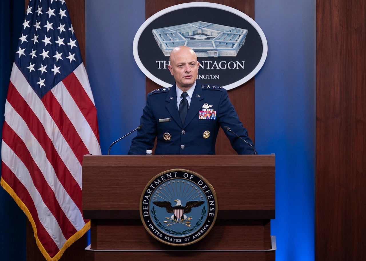 A man in a uniform stands at a lectern and speaks. A sign in the background indicates that he is at the Pentagon.