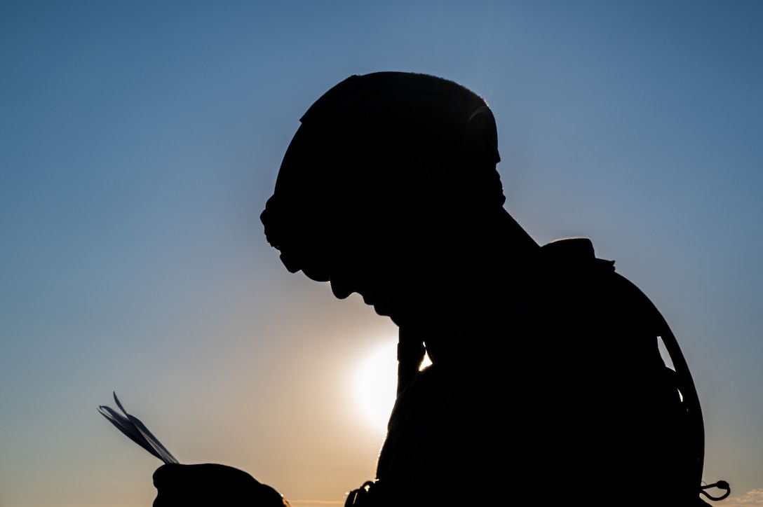 An airman looks at an object in his hands as shown in silhouette.