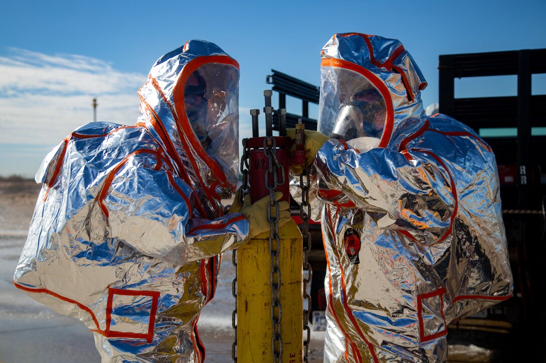 Two Marines in protective gear work on a gas tank.