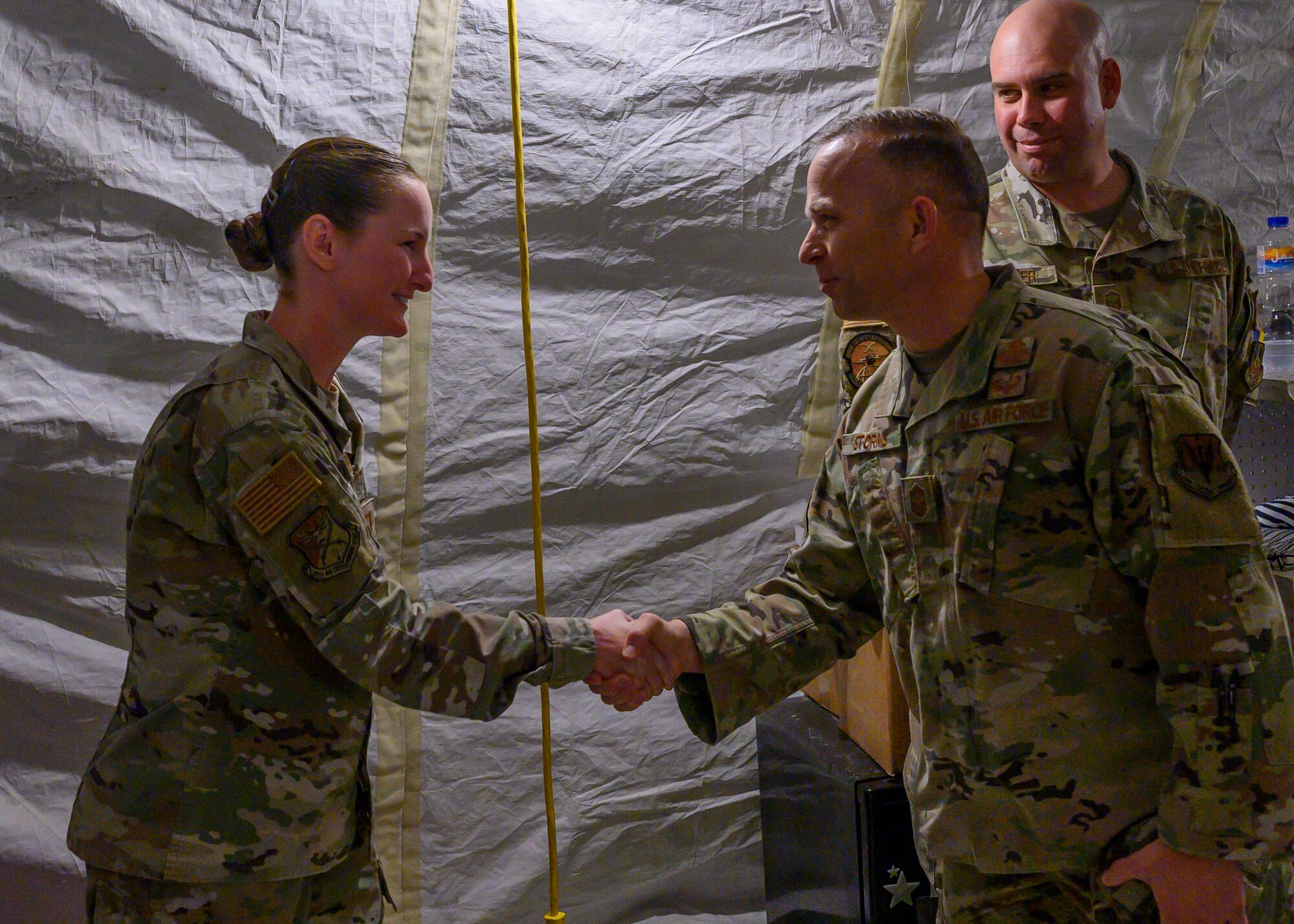 U.S. Air Force Chief Master Sgt. John Storms, 9th Air Force (Air Forces Central) command chief, shakes hands with U.S. Air Force Capt. Samantha Belo, 378th Expeditionary Medical Group executive officer, after she was recognized for her commitment to excellence and recent efforts in strengthening the relationship with local Saudi Arabian medical organizations, Prince Sultan Air Base, Kingdom of Saudi Arabia, Oct. 31, 2021. Storms joined U.S. Air Force Lt. Gen. Greg Guillot, 9th AF (AFCENT) commander, for a visit to several units across PSAB, meeting with various personnel to learn about recent innovation, diversity and expansion efforts on base. (U.S. Air Force photo by Senior Airman Samuel Earick)