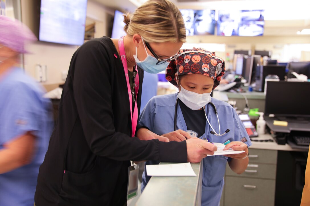 Two women, one wearing a mask, and one wearing a face mask and surgical cap, review an ER schedule.