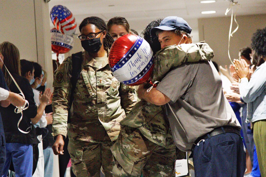 Several soldiers wearing face masks receive a reverse joint reception while one of the soldiers hugs a man wearing a face mask.