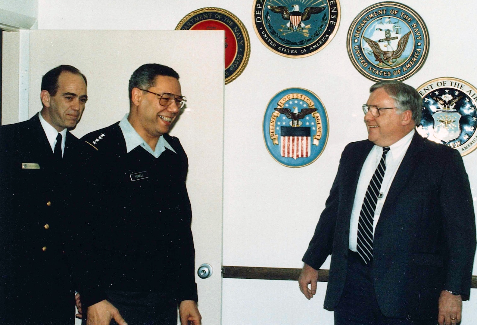 Male Navy Admiral and Army Gen. Colin Powell visit a civilian man during a 1991 visit to Cameron Station, Virginia.