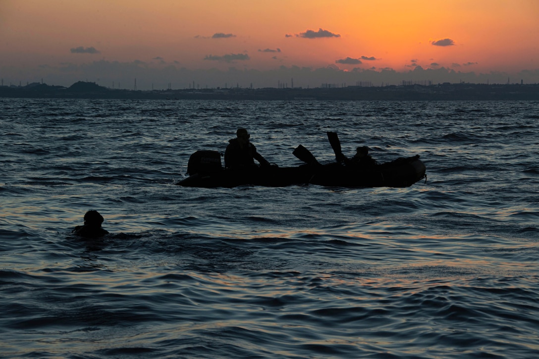 A Marine swims towards a small boat under a sunlit sky.