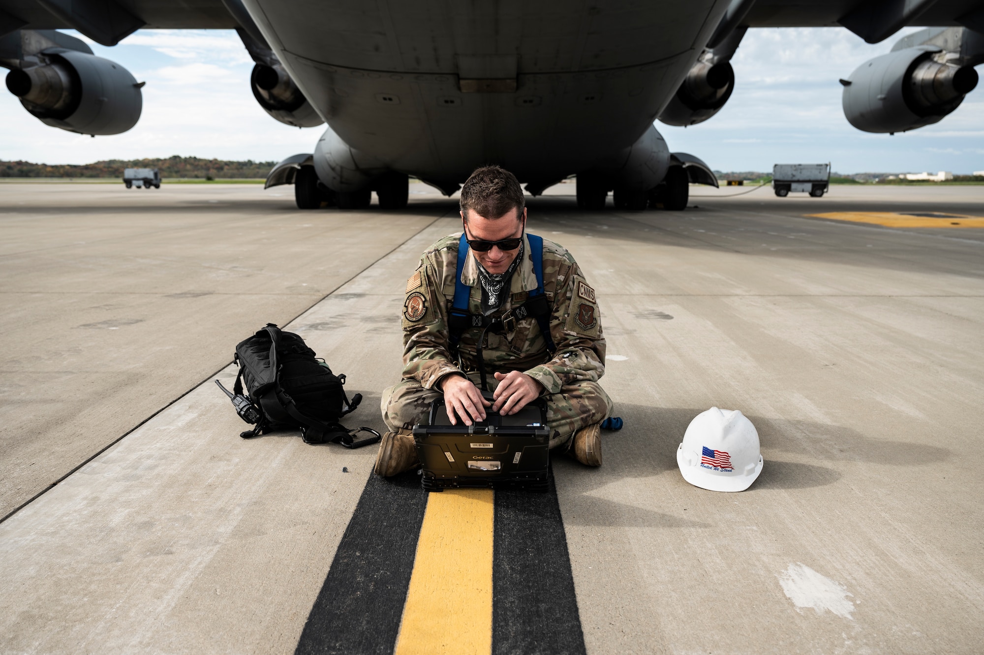 An Airman uses an iPad while sitting in front of a large aircraft