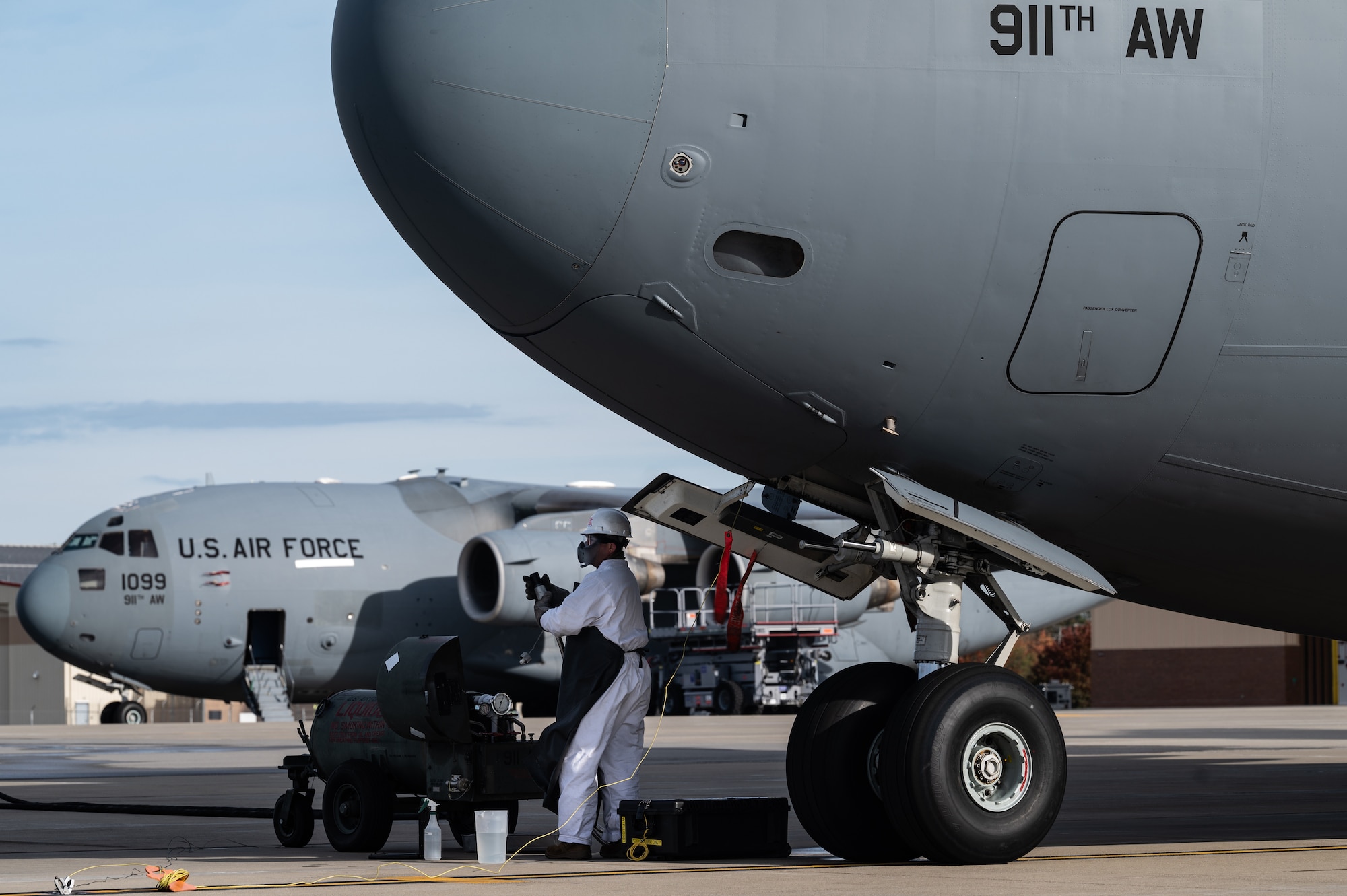 An Airman in a white suit stands in front of a large aircraft