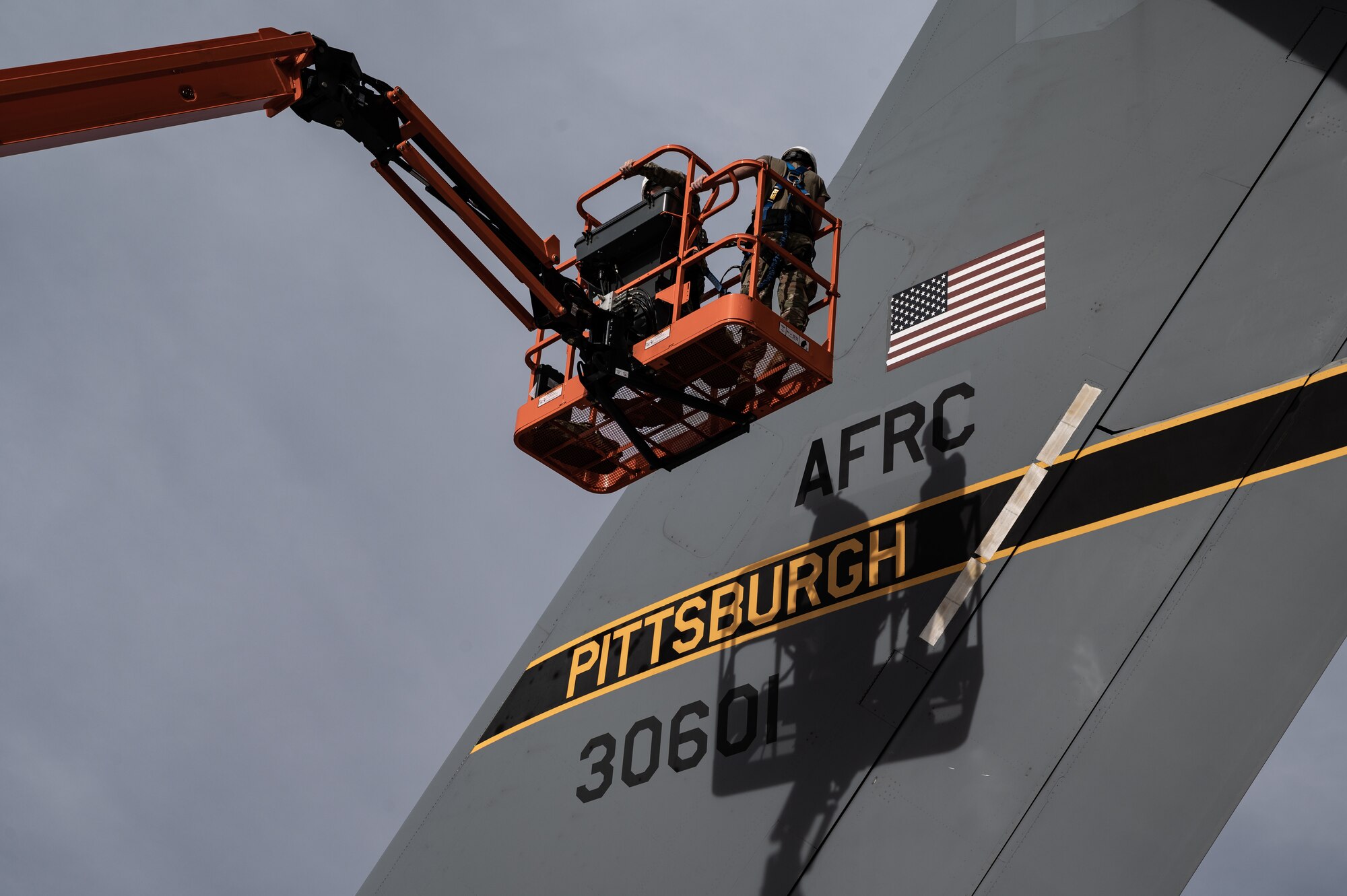 An Airman stands in an orange cherry picker in front of an aircraft tail that reads "Pittsburgh"