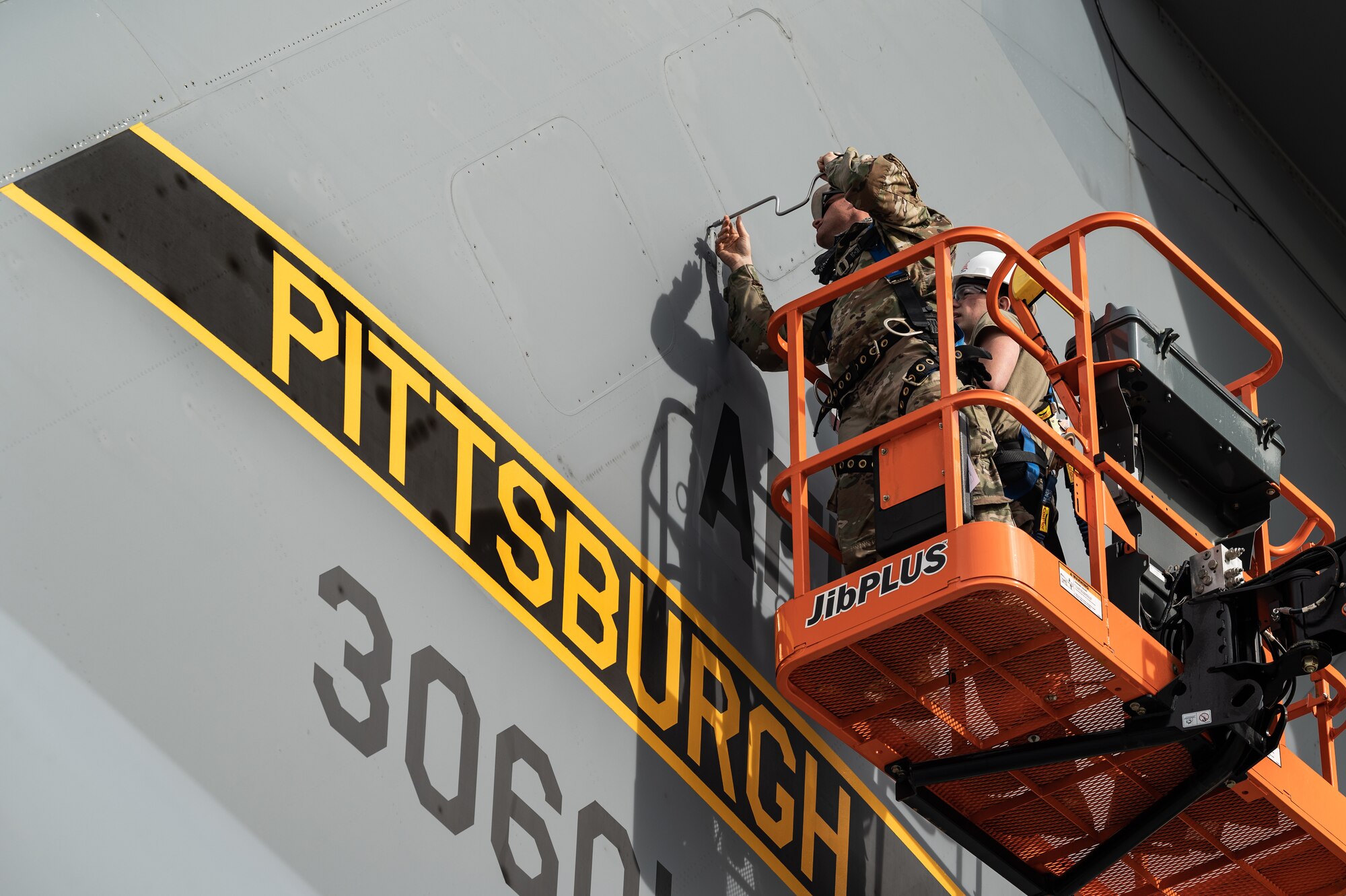 An Airman stands in an orange cherry picker while working on an aircraft tail that reads "Pittsburgh"