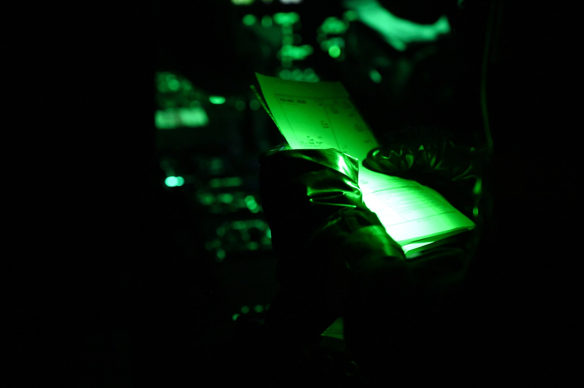 A pilot reads mission notes which are illuminated in green in the cockpit.