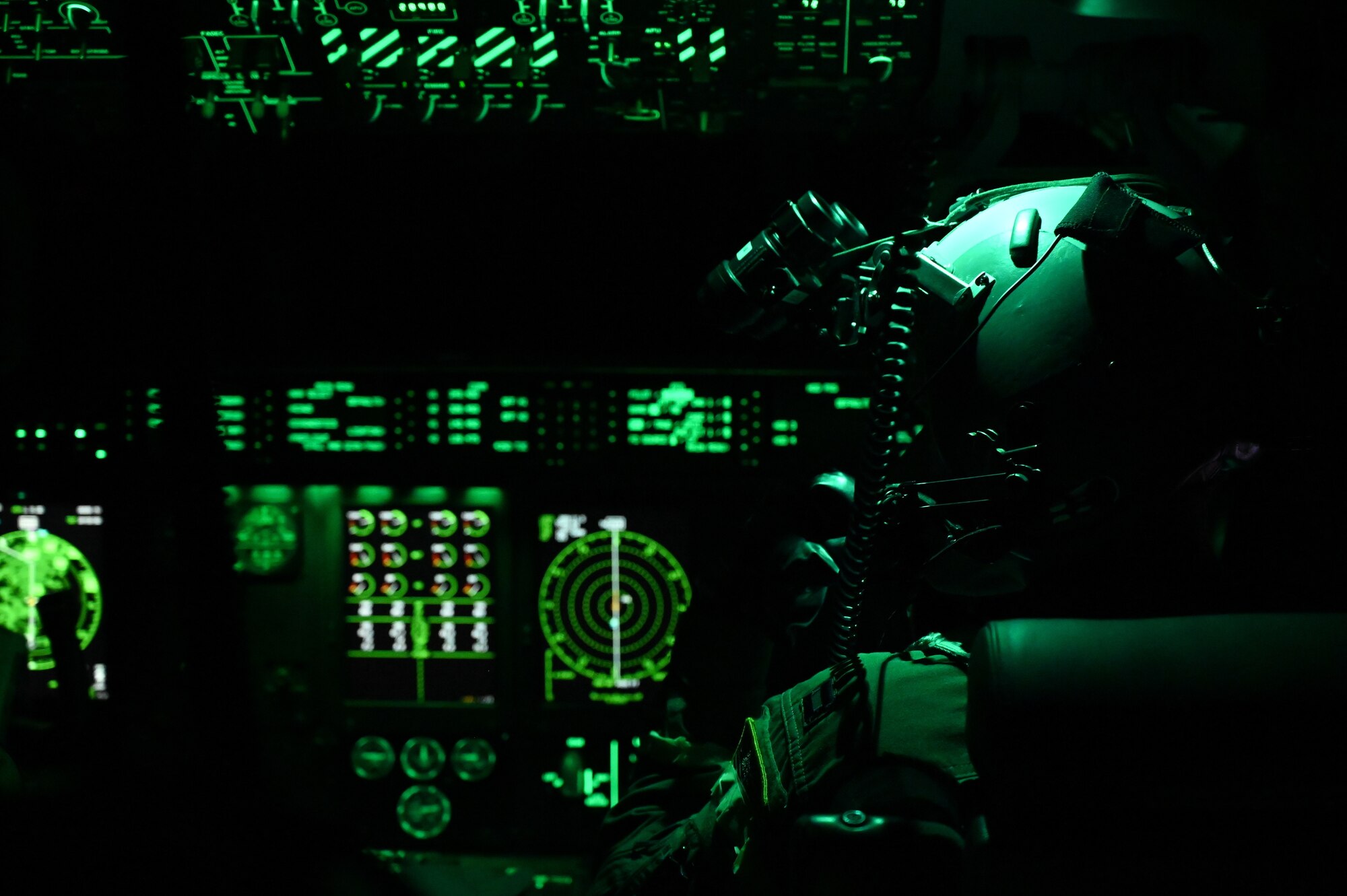 A pilot flies at night in an illuminated green cockpit.